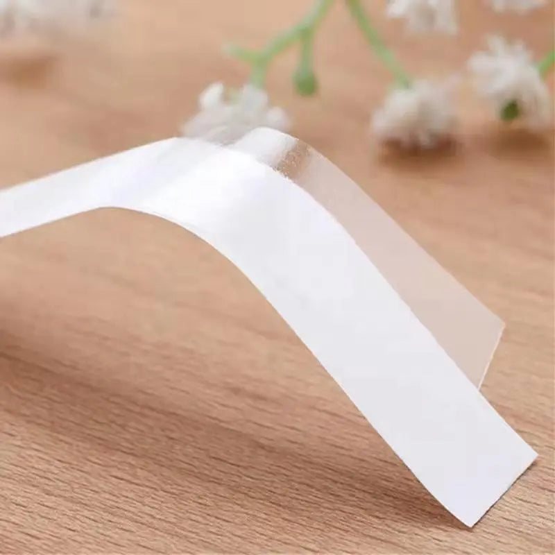 Miếng keo trong suốt, cong nhẹ trên nền gỗ, có hoa trắng mờ ở hậu cảnh.