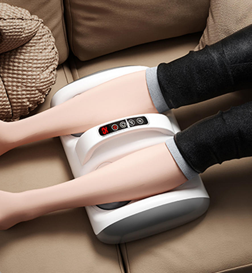 Máy massage chân màu trắng, hiển thị đèn LED đỏ, đặt trên ghế sofa nâu.