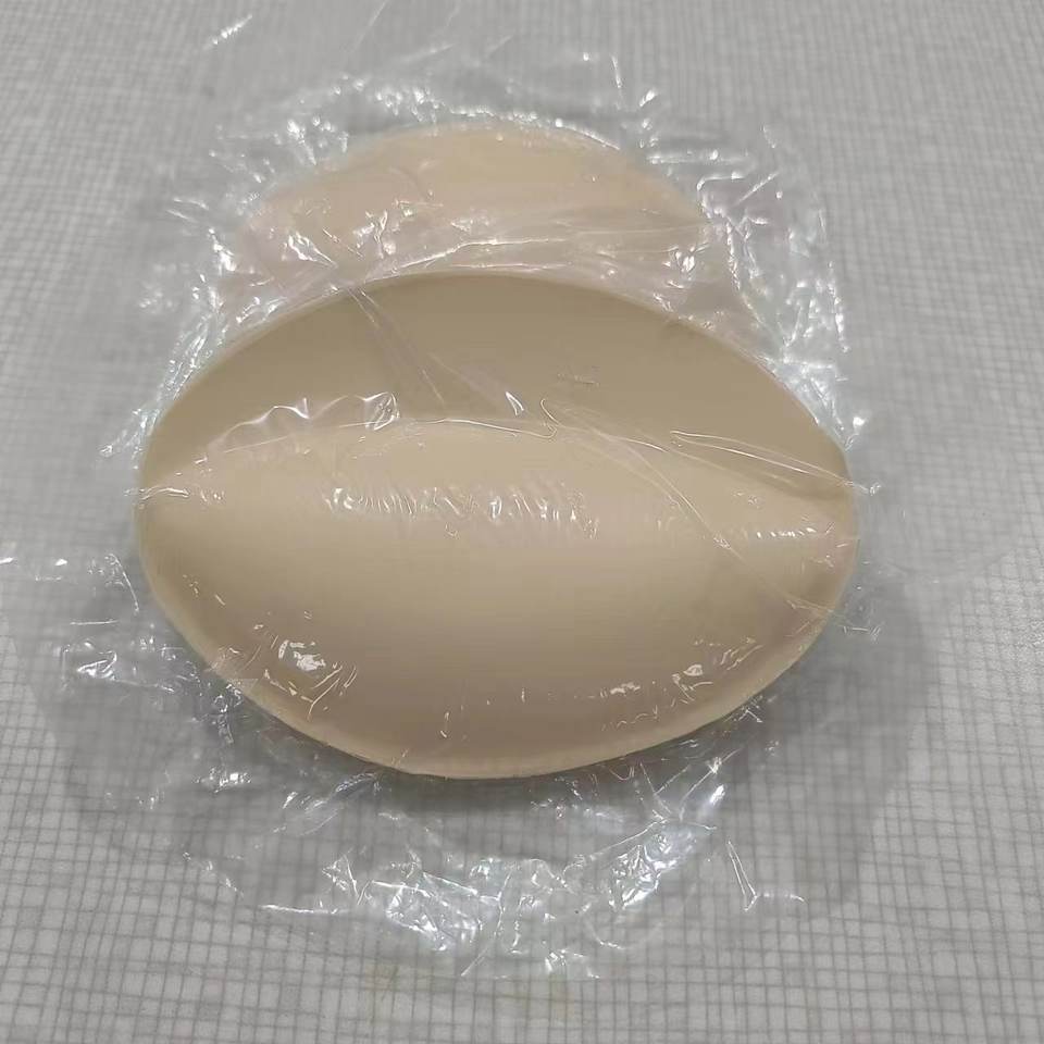 Hai miếng đệm mút màu da gói trong nilon, đặt trên bề mặt màu xám nhạt.