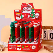 Bộ bút Giáng Sinh trên giá đỡ đỏ, có hình ông Noel và cây thông, màu xanh lá và đỏ nổi bật.