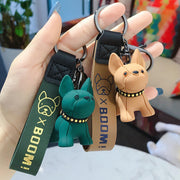 Móc khóa với hai chú chó màu xanh lá cây và cam, dây đeo xanh và nâu có chữ "BOOM!".