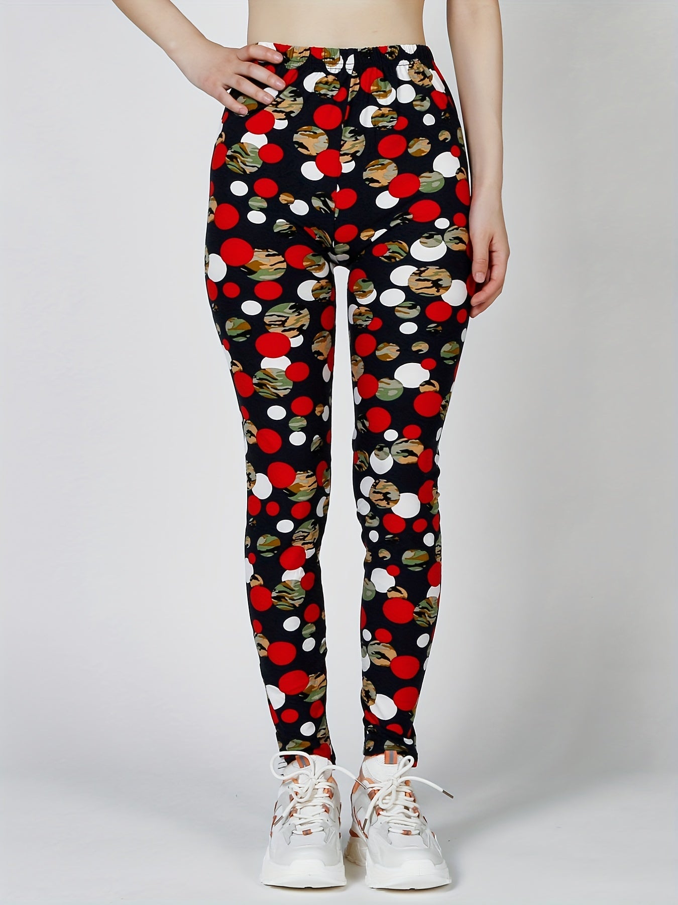 Quần legging đen hoạ tiết chấm tròn đỏ, trắng, rằn ri. Người mẫu đi giày thể thao trắng.