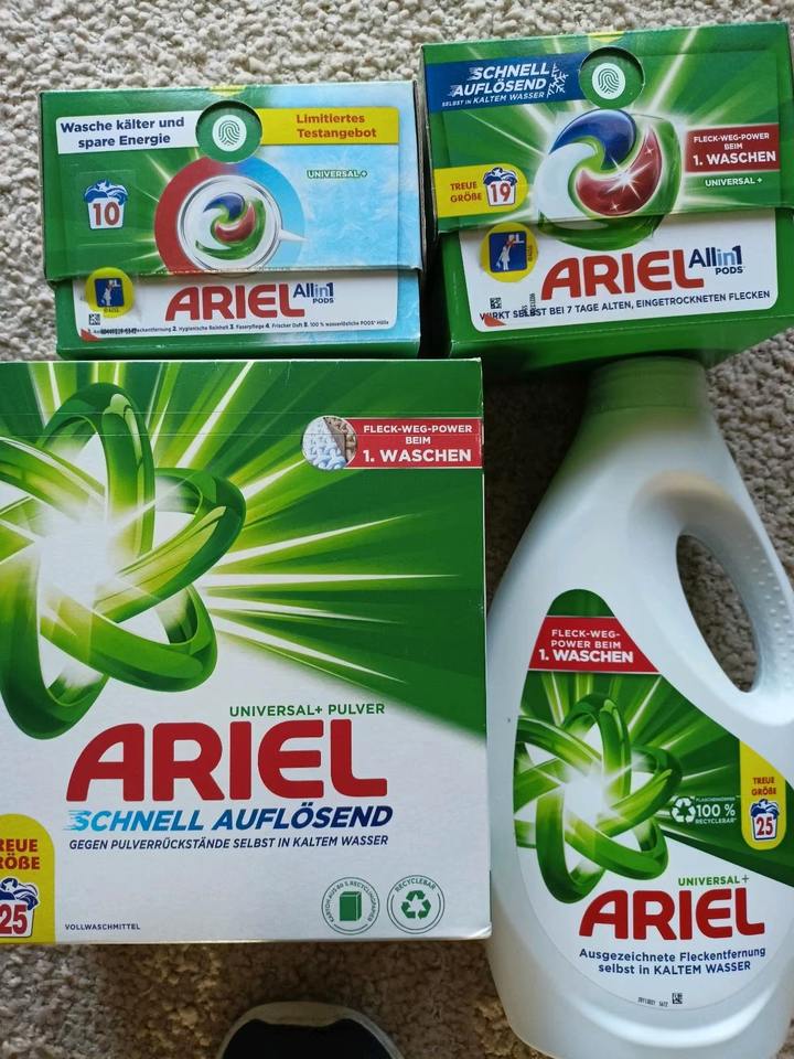 Các hộp và chai bột giặt Ariel, nền xanh lá cây, chữ trắng và đỏ nổi bật.