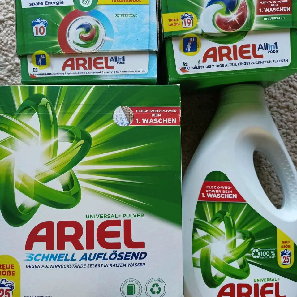 Các hộp và chai bột giặt Ariel, màu xanh lá và trắng, với logo xoáy nổi bật.