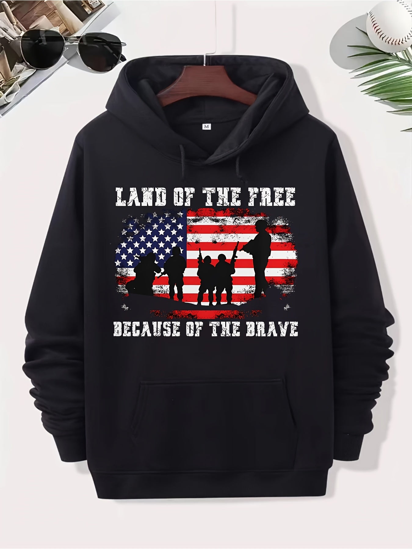 Áo hoodie đen in cờ Mỹ, bóng dáng quân nhân và chữ trắng: "Land of the Free, Because of the Brave".