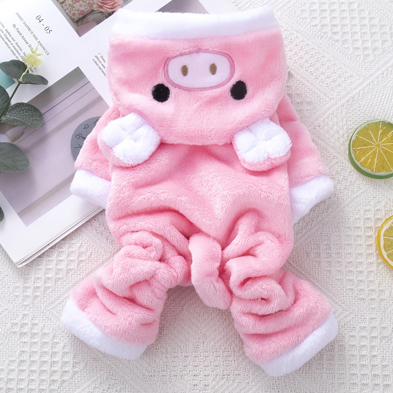 Bộ trang phục thú bông hồng hình heo, viền trắng, nằm trên nền vải và tạp chí.