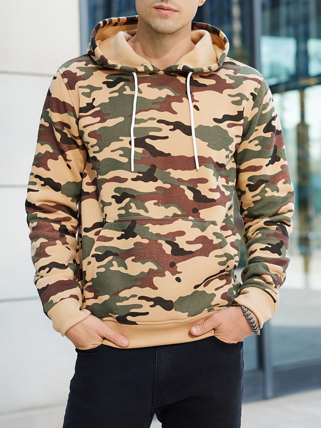 Người mặc áo hoodie họa tiết rằn ri xanh lá, nâu, be; quần đen; trong bối cảnh phố phường.