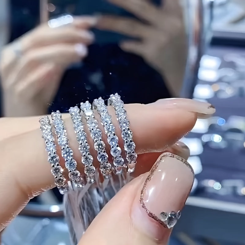 Một bàn tay cầm nhiều nhẫn kim cương sáng lấp lánh, nền sau mờ với ánh sáng lấp lánh.
