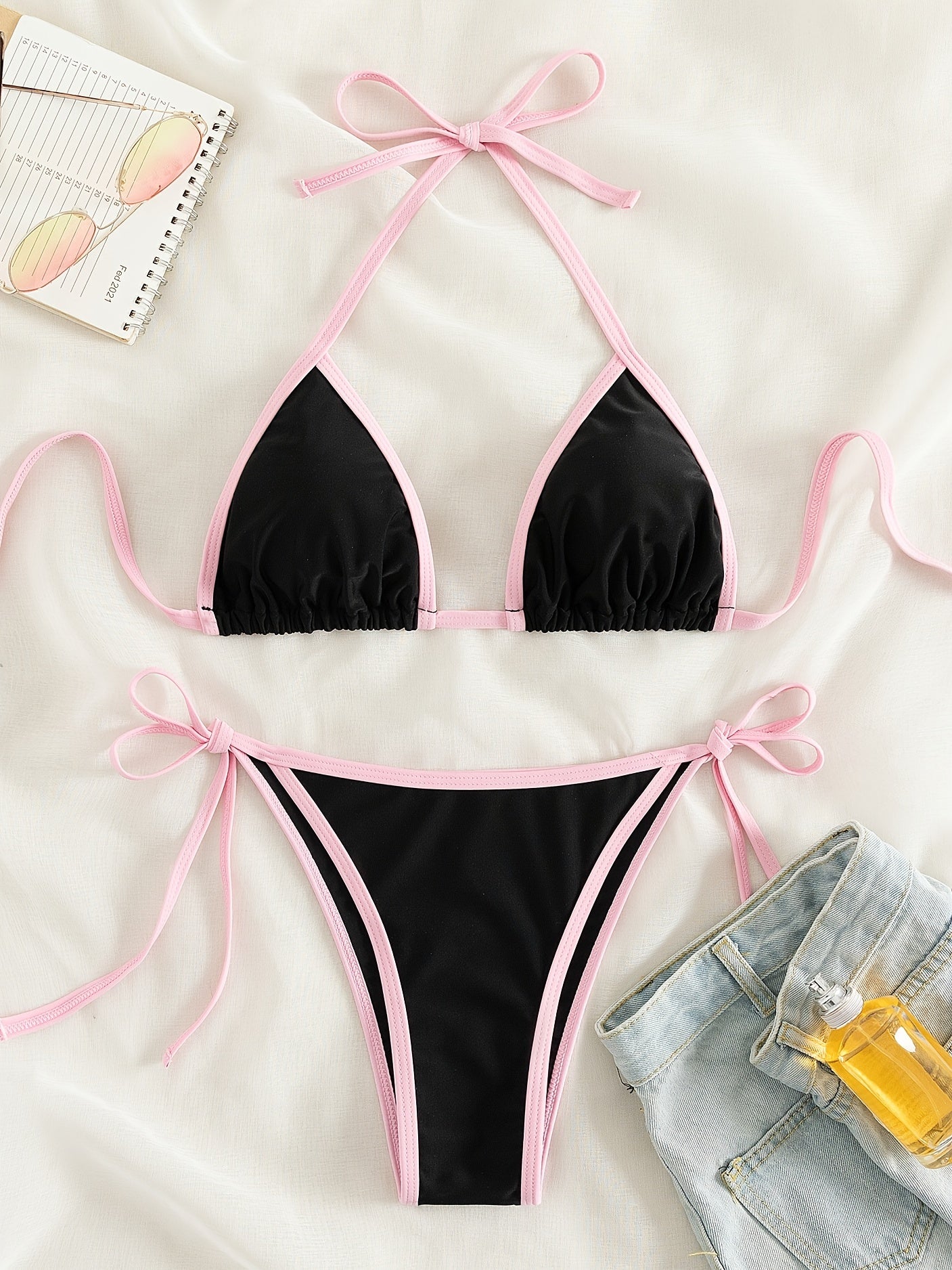 Bikini màu đen viền hồng trên nền trắng, bên cạnh có quần short jean, sổ và kính râm.