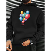 Áo hoodie đen có hình in chùm bóng bay nhiều màu sắc, nền là bức tường sọc ngang.