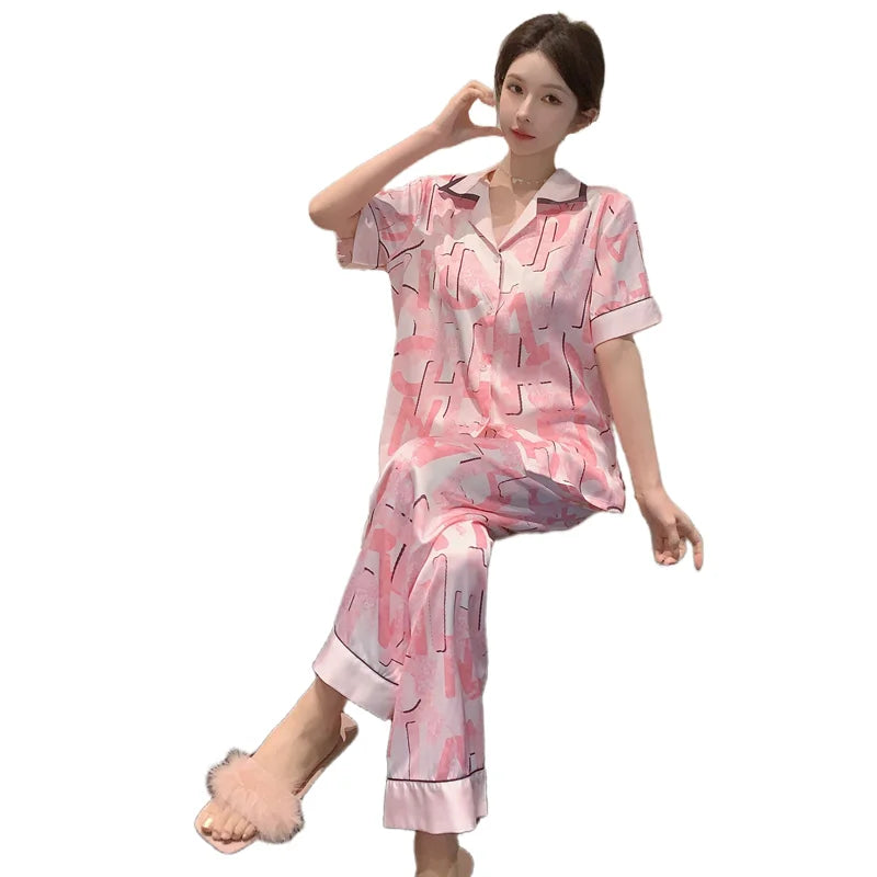 Người phụ nữ mặc đồ ngủ hồng họa tiết chữ, đi dép lông, ngồi trên nền trắng.
