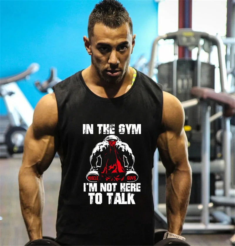 Người đàn ông mặc áo đen với chữ trắng, tập gym, nền xanh da trời và thiết bị thể dục.