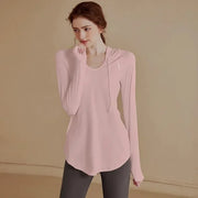 Người phụ nữ mặc áo hồng dài tay, dạng hoodie, quần tối màu, đứng trên nền màu be.