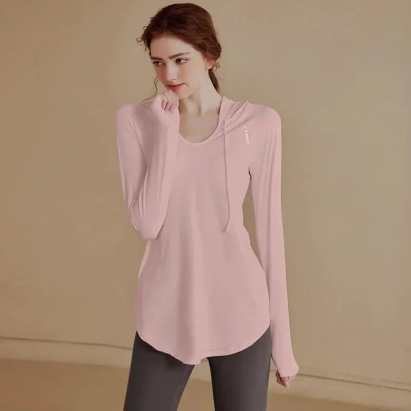 Người phụ nữ mặc áo hồng dài tay, dạng hoodie, quần tối màu, đứng trên nền màu be.