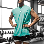 Người mặc áo xanh ngọc, quần đen, đứng trong phòng gym, tay chống hông, ánh sáng từ cửa sổ.