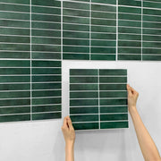 Tay đang cầm gạch màu xanh đậm, hình chữ nhật, nền tường trắng.