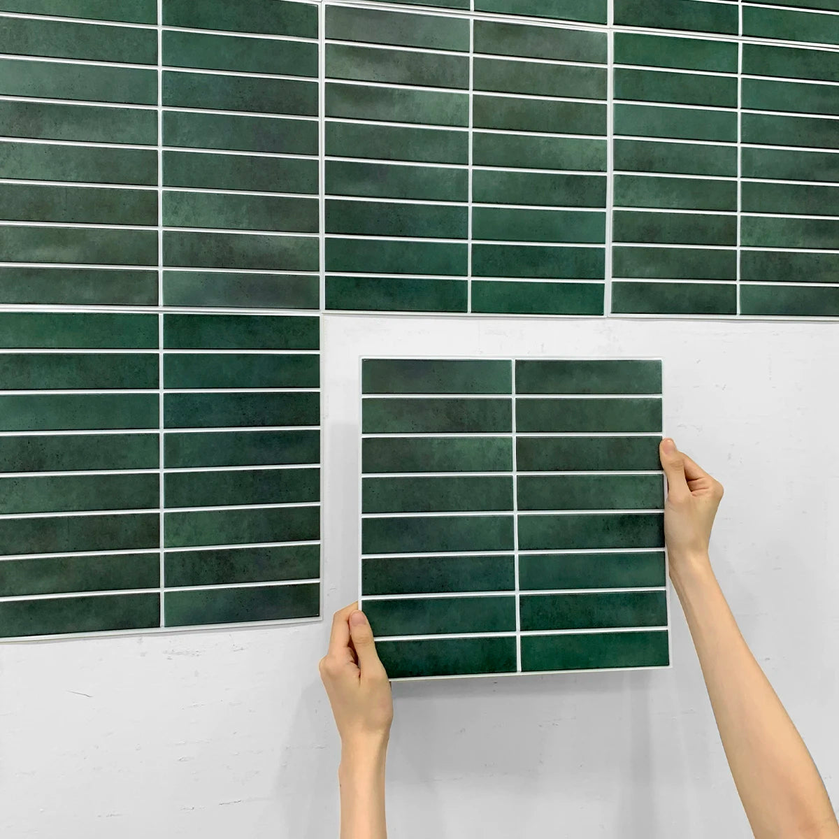 Tay đang cầm gạch màu xanh đậm, hình chữ nhật, nền tường trắng.