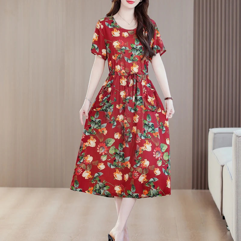 Người phụ nữ mặc váy dài đỏ họa tiết hoa lá, đứng trên nền nhà màu nâu nhạt.