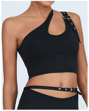 Áo crop top đen lệch vai, dây đai kim loại, kết hợp với quần đai mảnh, nền trắng nhạt.