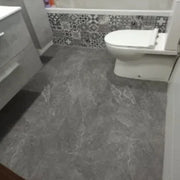 Nhà vệ sinh với sàn đá xám, tường gạch hoa văn đen trắng, bồn cầu trắng.