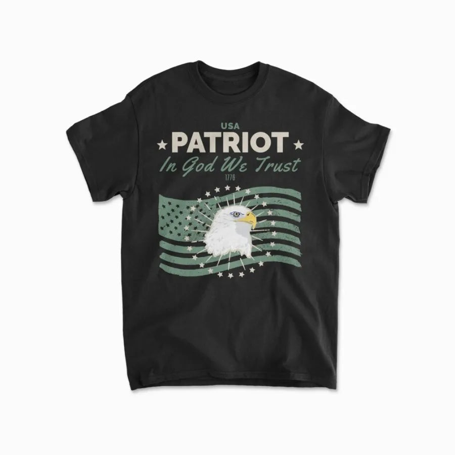 Áo thun đen với hình đại bàng, cờ Mỹ và chữ "Patriot, In God We Trust, 1776" màu trắng-xanh.