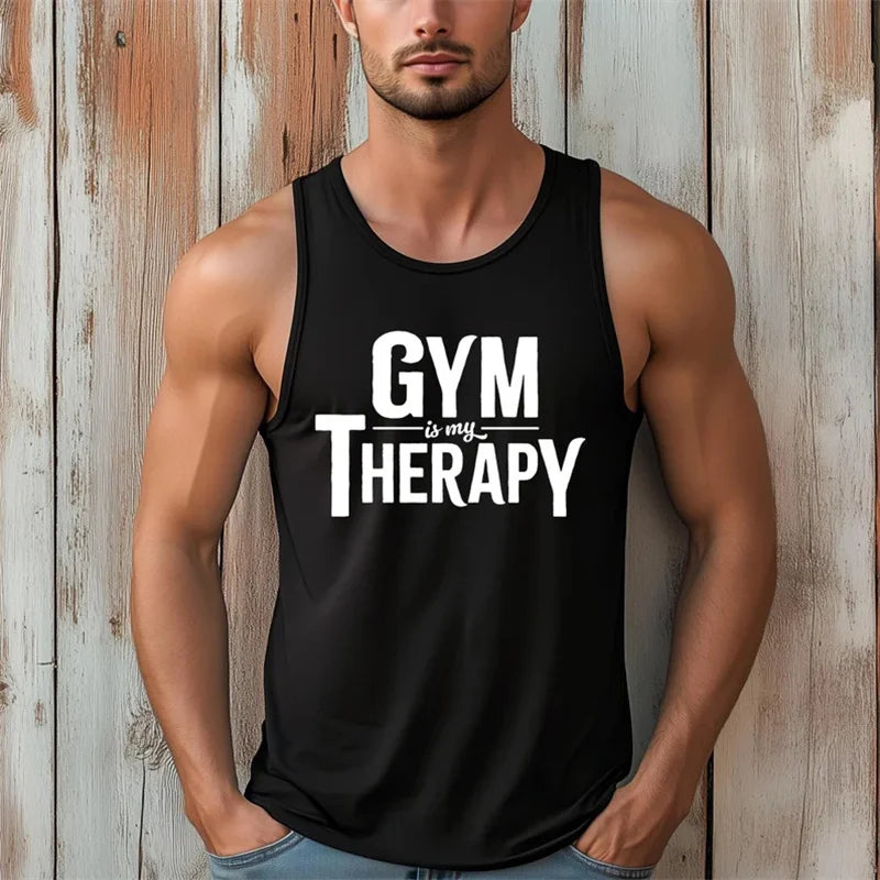 Người đàn ông mặc áo ba lỗ đen in chữ trắng "GYM is my THERAPY", đứng trước nền gỗ xám nâu.