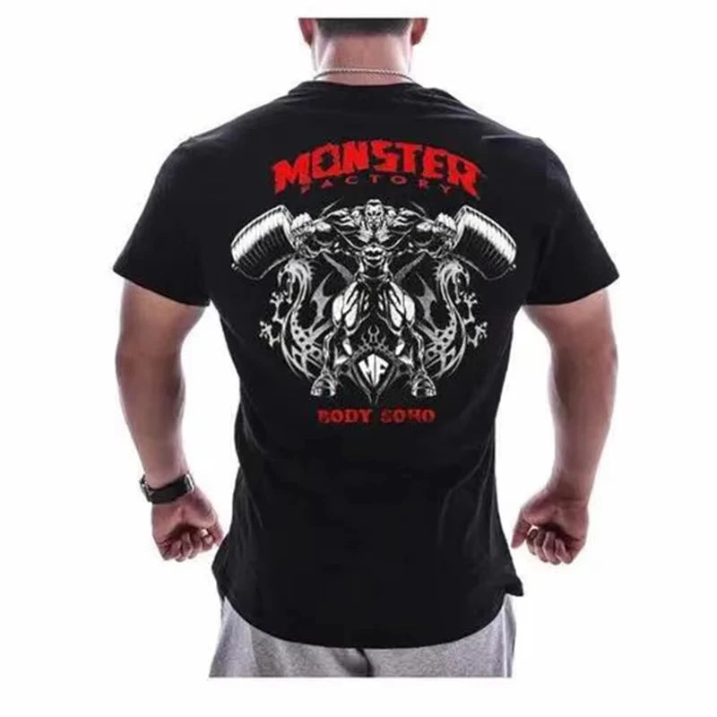 Áo thun đen với hình minh họa quái vật cầm tạ, chữ đỏ "Monster Factory Body Soho" phía sau.