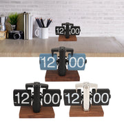 Bốn đồng hồ lật số trên đế gỗ, nền gạch trắng, có sách, máy ảnh và cốc bút.