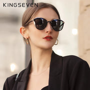 Người phụ nữ đeo kính râm đen, mặc áo khoác đen, bông tai vòng, nền mờ nhạt.
