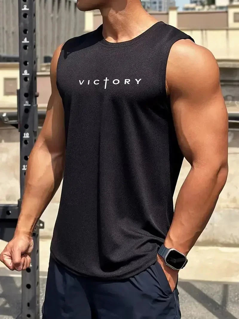 Người đàn ông mặc áo ba lỗ đen in chữ "VICTORY", đứng ngoài trời với cánh tay cơ bắp.