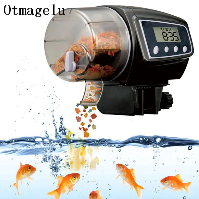 Máy cho cá ăn tự động màu đen, thức ăn rơi xuống bể với nước và cá vàng bơi lội.