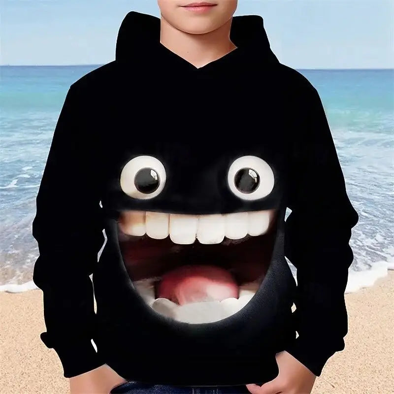 Người mặc áo hoodie đen có họa tiết mặt cười to, nền biển xanh và cát vàng.
