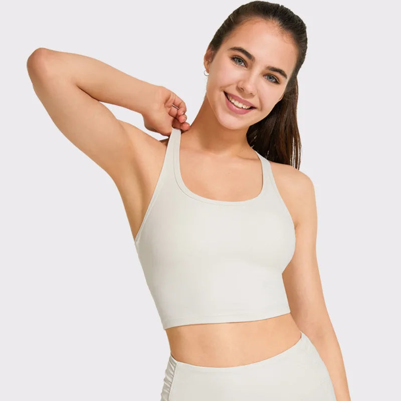 Người phụ nữ mặc áo thể thao màu kem, cười, tay trái đặt sau đầu, nền trắng.