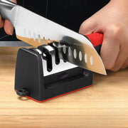 Tay cầm dao trên máy mài dao đen, lưỡi dao có vết cắt hình tròn, nền gỗ sáng.