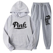 Bộ đồ thể thao xám, áo hoodie và quần dài có chữ "Pink" đen trên ngực và ống quần.