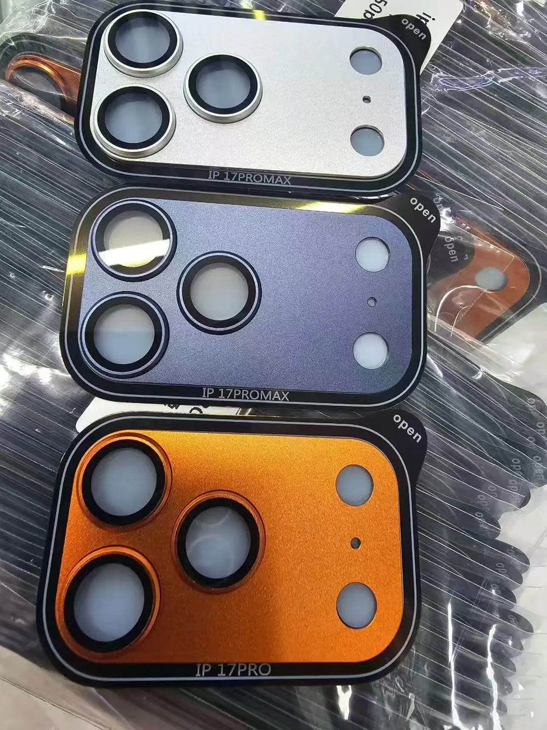 Ba ốp camera hình chữ nhật cho điện thoại, màu bạc, xanh và cam, có ba lỗ tròn lớn.