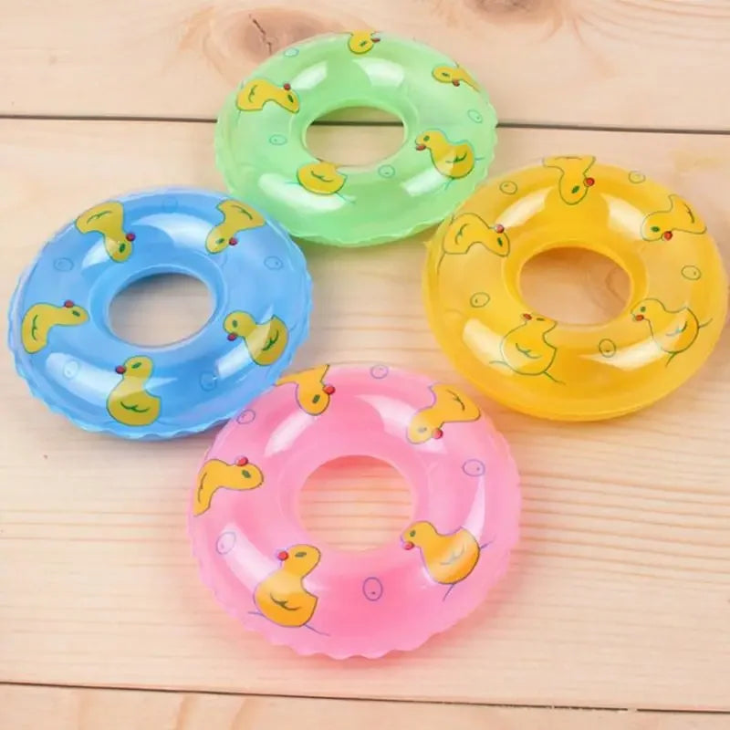 Bốn phao bơi tròn màu xanh lá, xanh dương, hồng, vàng có hình vịt nhựa, đặt trên nền gỗ.