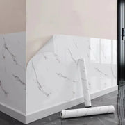 Tường phủ giấy dán vân đá trắng, hai cuộn giấy đặt trên sàn xám bóng.
