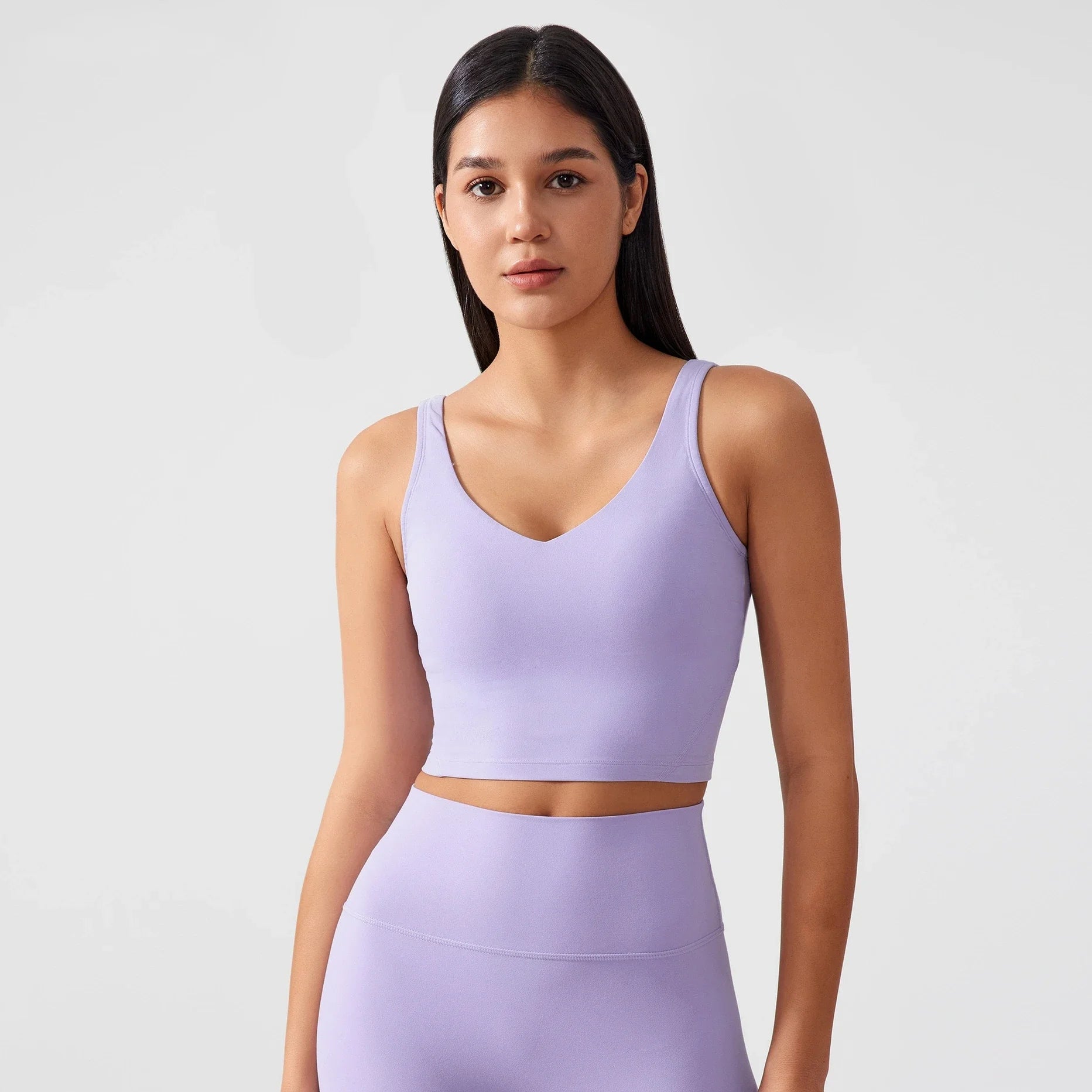Người mẫu mặc áo crop top và quần tập màu tím nhạt, tóc đen dài, nền trắng.