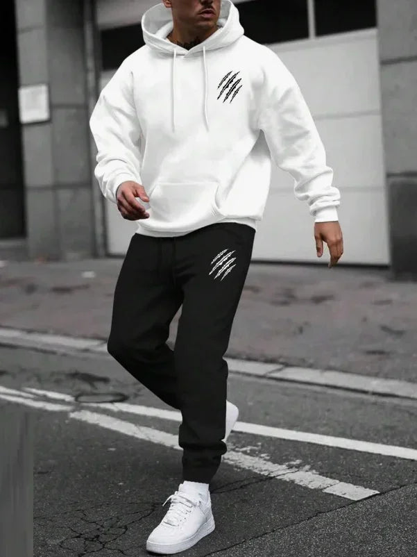 Người mặc áo hoodie trắng, quần đen có họa tiết trắng, đi giày thể thao trắng trên phố.