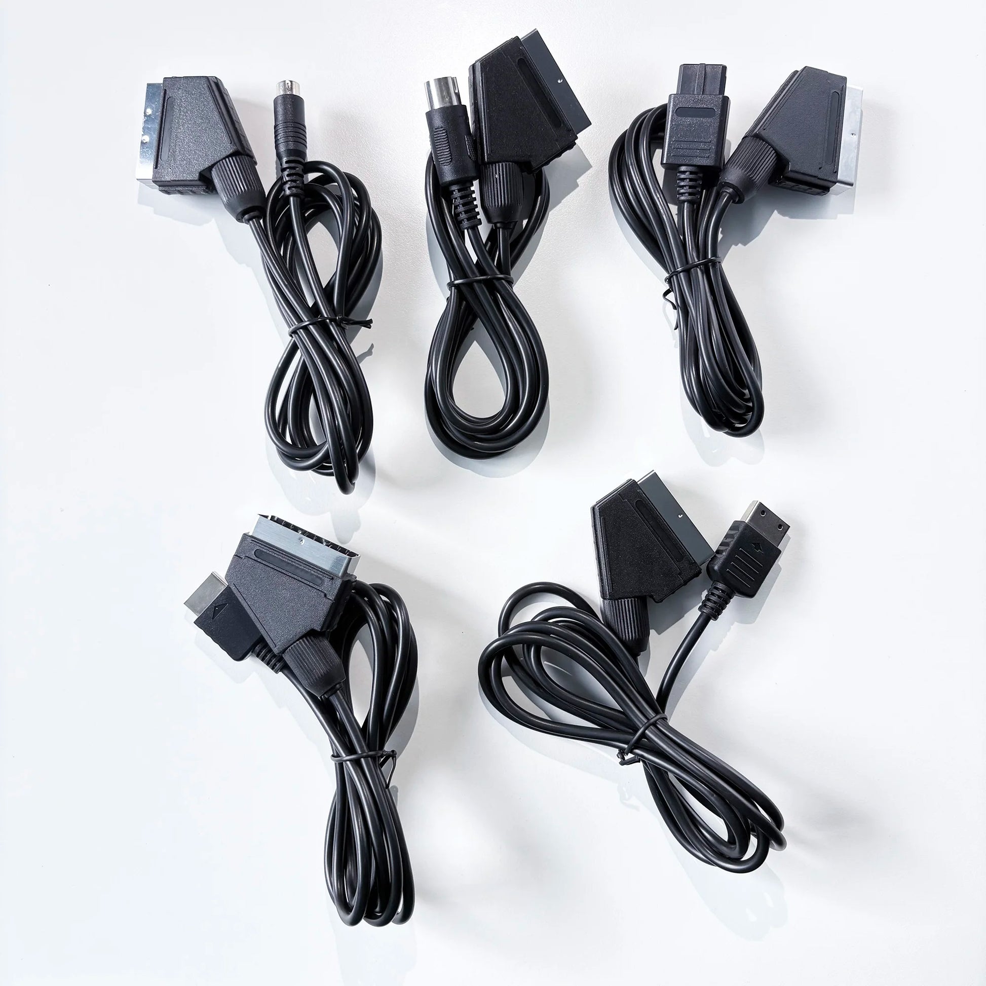 Năm sợi cáp đen với đầu nối SCART và RCA trên nền trắng.