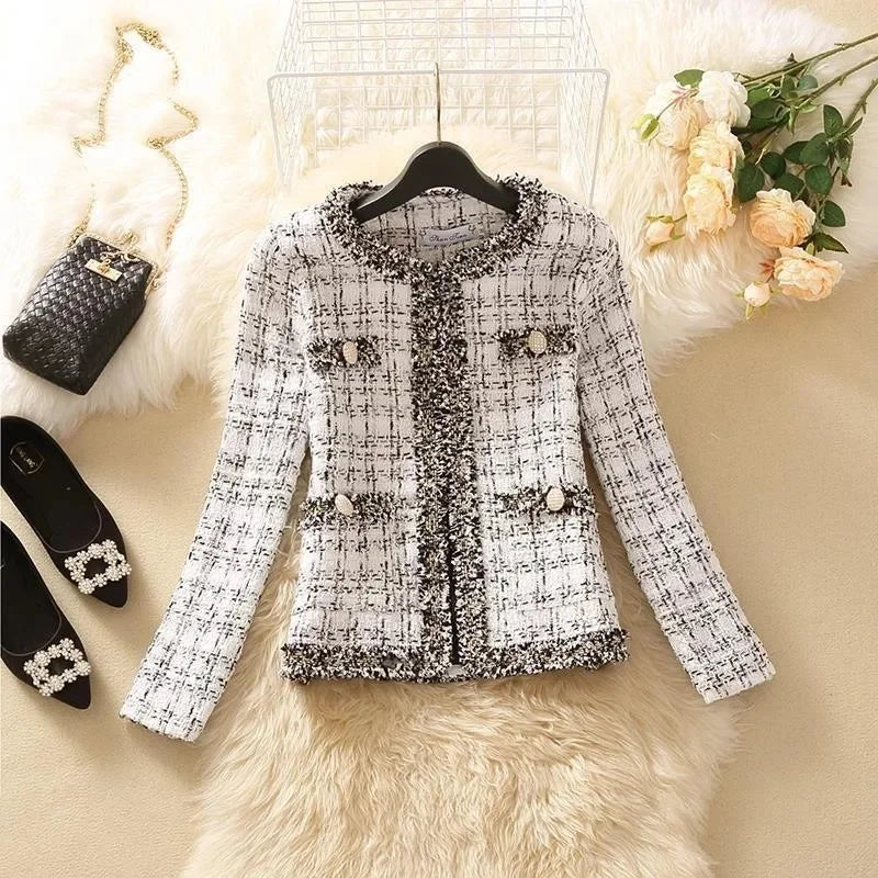 Áo khoác vải tweed trắng đen, túi nút, nằm trên thảm lông, cạnh hoa hồng và túi xách đen.