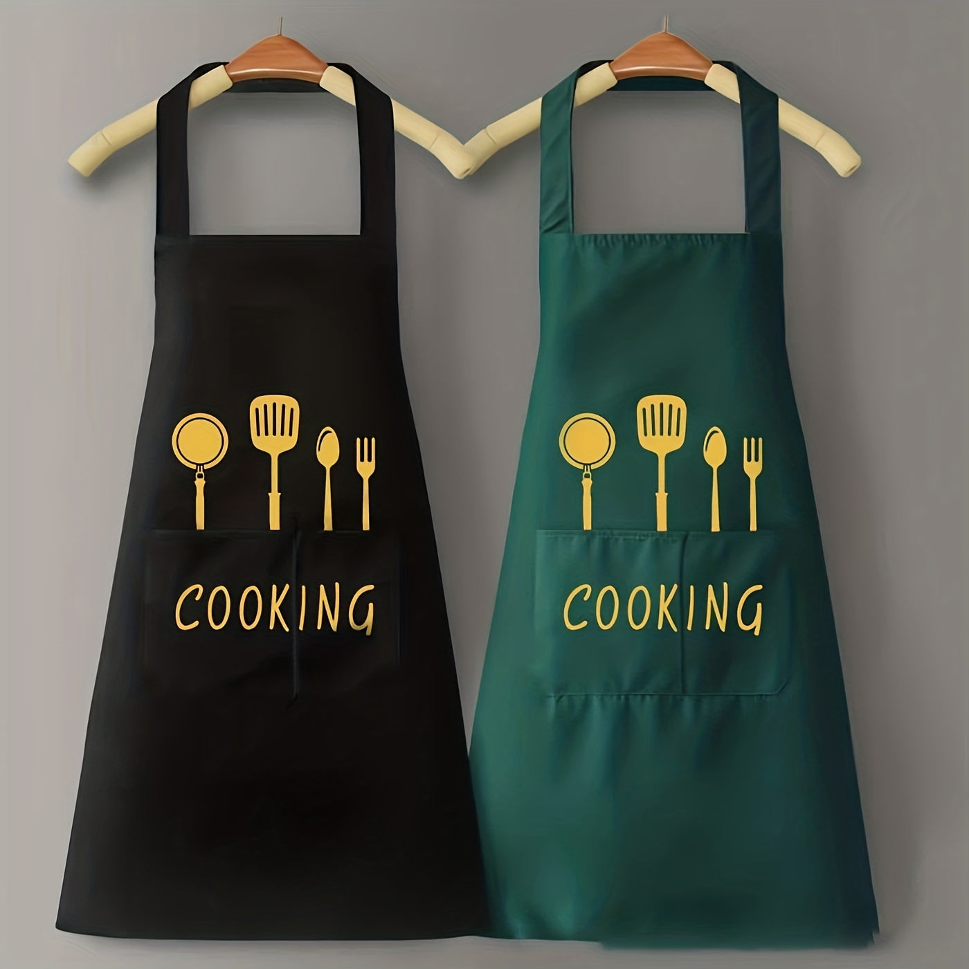 Hai tạp dề, một đen một xanh, in hình dụng cụ nấu ăn và chữ "COOKING" màu vàng.