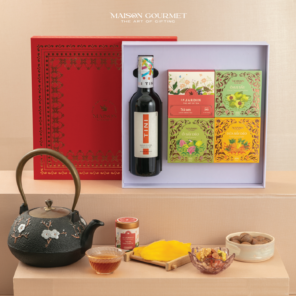 Hộp quà với chai rượu vang, ba hộp trà, ấm trà đen, mứt và khay bánh màu vàng.