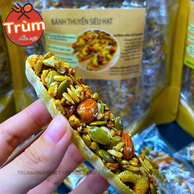 Người cầm bánh gạo có nhiều loại hạt màu sắc, nền có bao bì in chữ và hình ảnh sản phẩm.