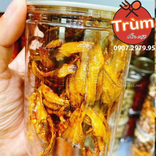 Hũ cá khô vàng óng ánh trong suốt, cầm tay, nắp nhựa. Hình ảnh có logo và số điện thoại bên phải.