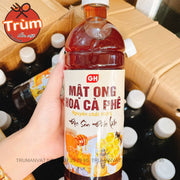 Chai mật ong hoa cà phê màu nâu sẫm với nhãn trắng và chữ đỏ, trên tay người cầm.
