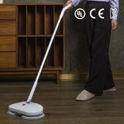 Người sử dụng cây lau nhà điện màu trắng trên sàn gỗ, cạnh kệ gỗ, logos chứng nhận phía trên.