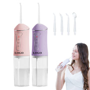 Máy tăm nước màu hồng và tím, kèm 5 đầu phun. Cô gái sử dụng máy, mặc váy trắng.