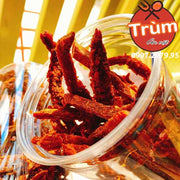 Hũ đựng khô bò sợi màu đỏ tươi, nằm nghiêng trên nền vàng sáng, logo "Trùm Ăn Vặt" ở góc phải.